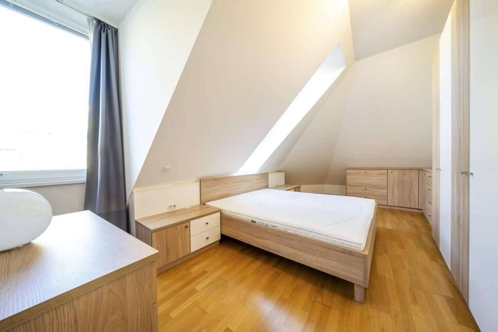 Helles Schlafzimmer mit Holzbett, Nachttischen, Schrank und Dachschrägenfenster.