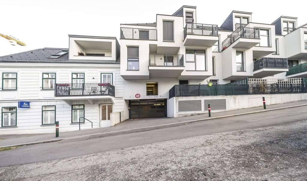 Moderne Wohnanlage mit Balkonen und Tiefgaragenzufahrt neben einem Altbaugebäude.