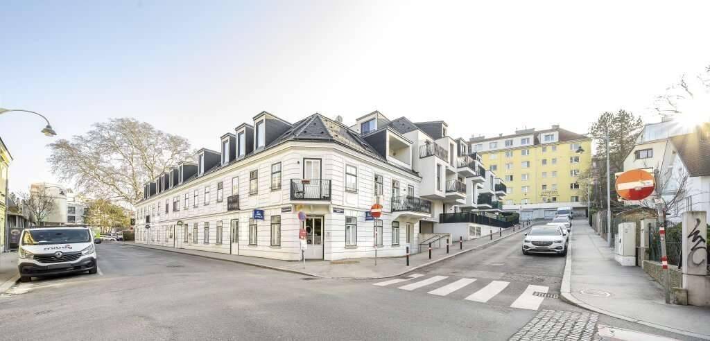 Straßenansicht des modernen Gebäudes an einer Ecke mit umliegender Bebauung und Bäumen.