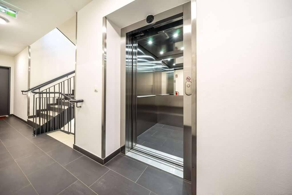 Heller Flur im Gebäude mit modernem Aufzug und Treppenhaus.