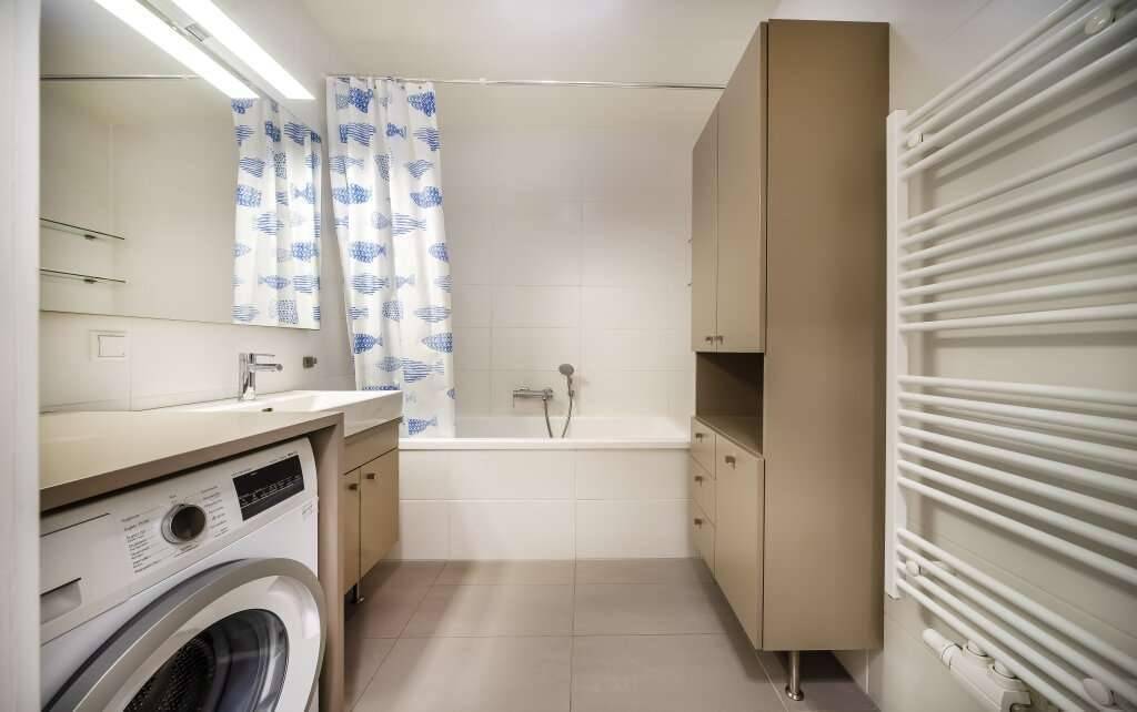 Helles Badezimmer mit Badewanne, Waschbecken, Waschmaschine und beheiztem Handtuchhalter.