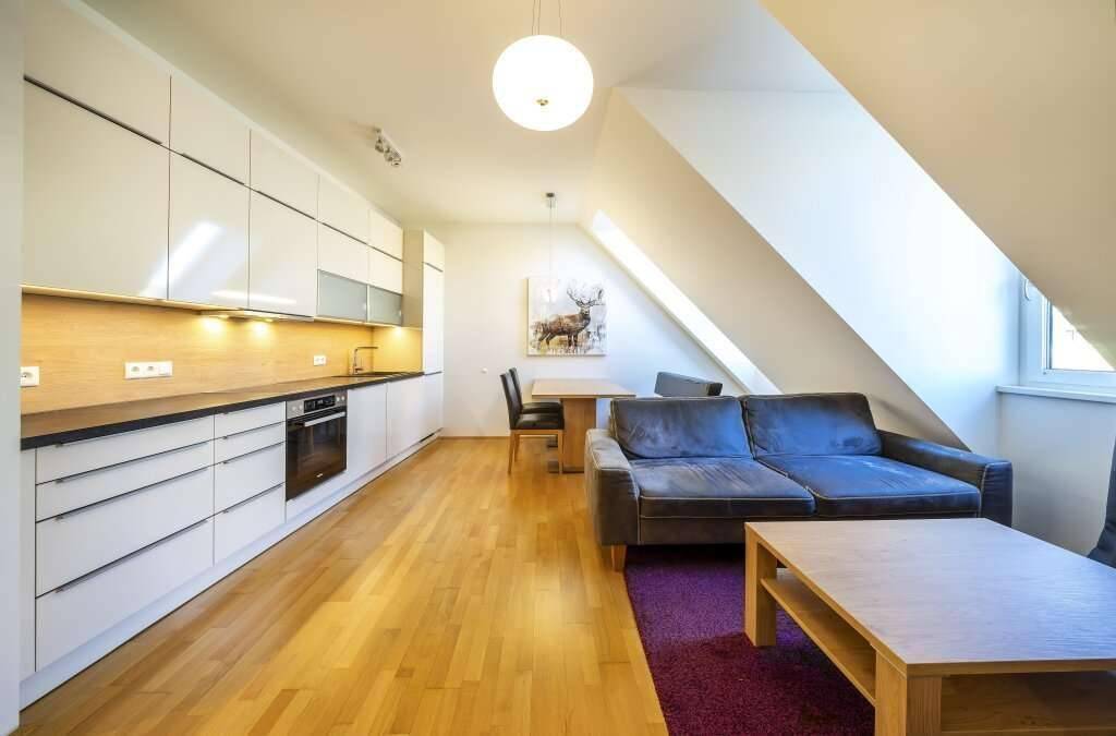 Moderner Wohnbereich mit integrierter Küche, Esstisch und gemütlichem Sofa unter der Dachschräge.
