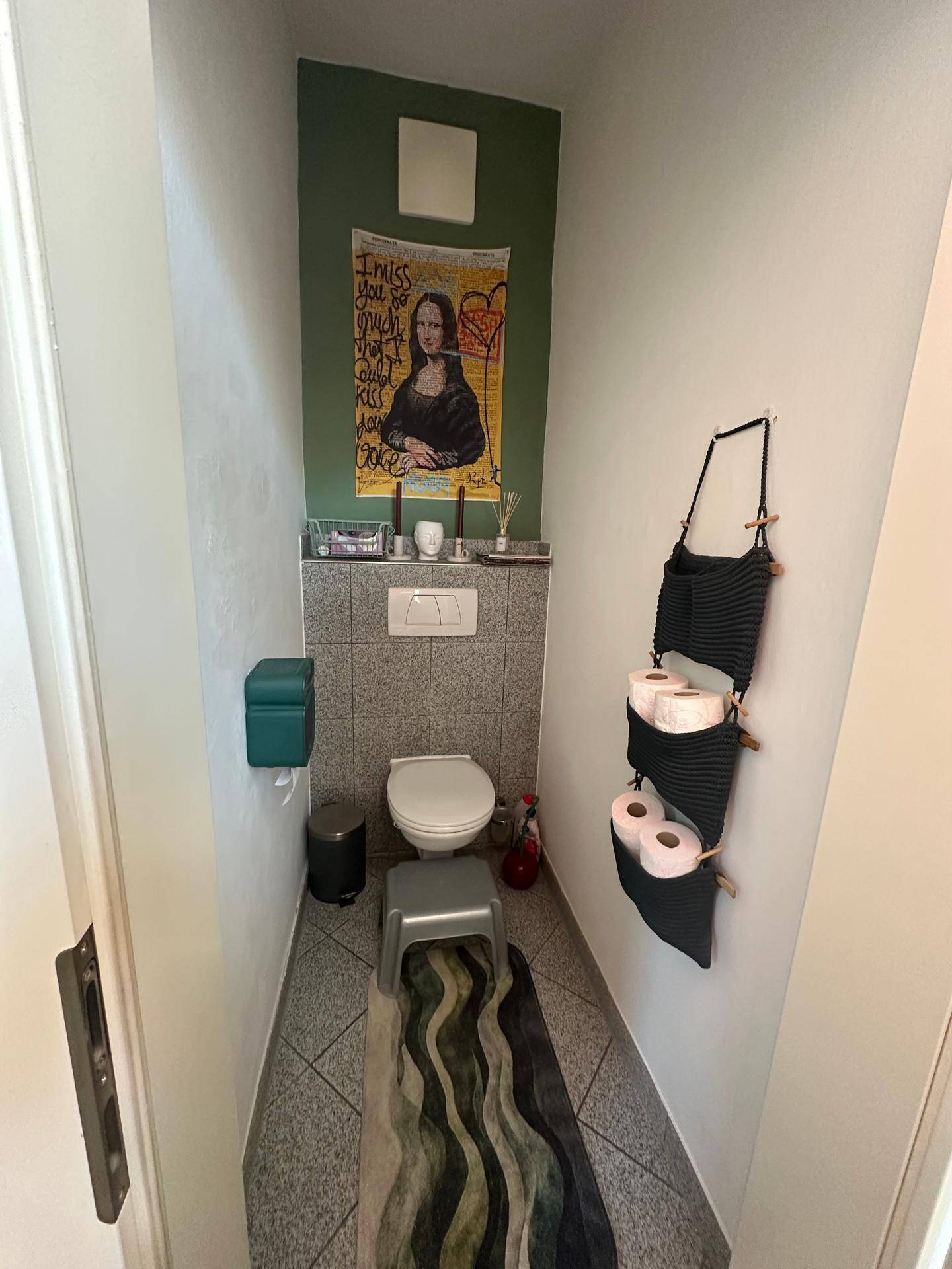 Schmale Gästetoilette mit Fliesenboden, Wand-WC und kreativer Wanddekoration.