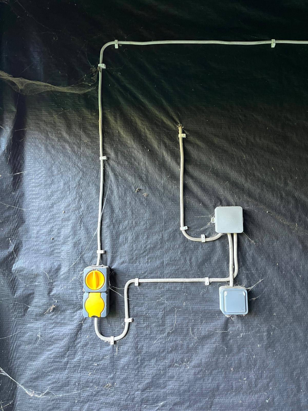 Elektrische Installationen mit Steckdosen und Kabeln an einer mit schwarzer Folie verkleideten Wand.