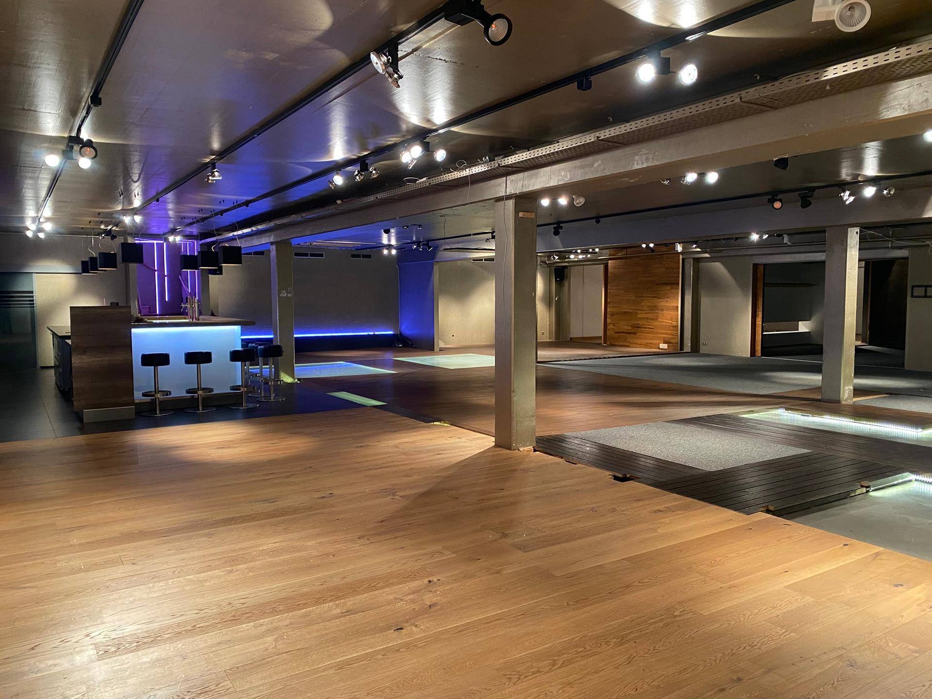 Geräumiger Veranstaltungsraum mit Holzboden, beleuchteter Bar und blauer Akzentbeleuchtung, ideal für Events.