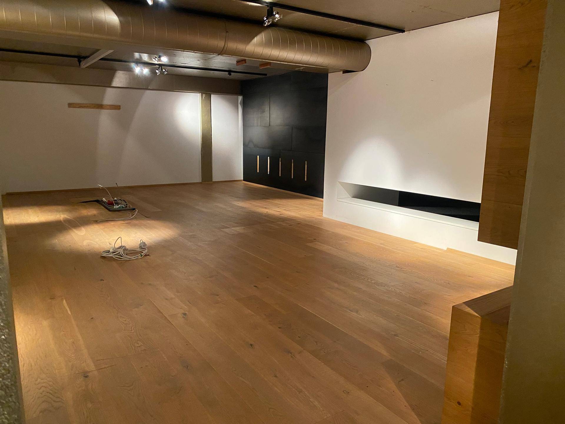 Moderner Lounge-Bereich mit Holzboden, dunkler Akzentwand und integriertem Kamin unter sichtbaren Rohren.