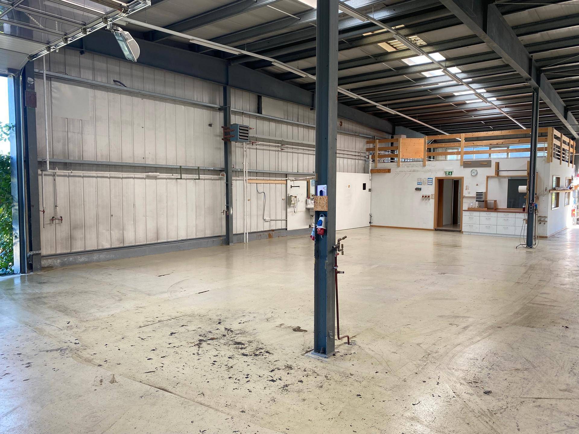 Weitläufige Lagerhalle mit Betonboden, sichtbaren Metallträgern und einer erhöhten Mezzanine-Ebene.