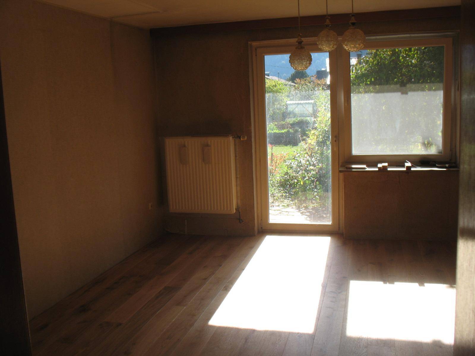 Heller Raum mit Holzboden, Heizkörper und direktem Zugang zum Gartenbereich, der Renovierung benötigt.