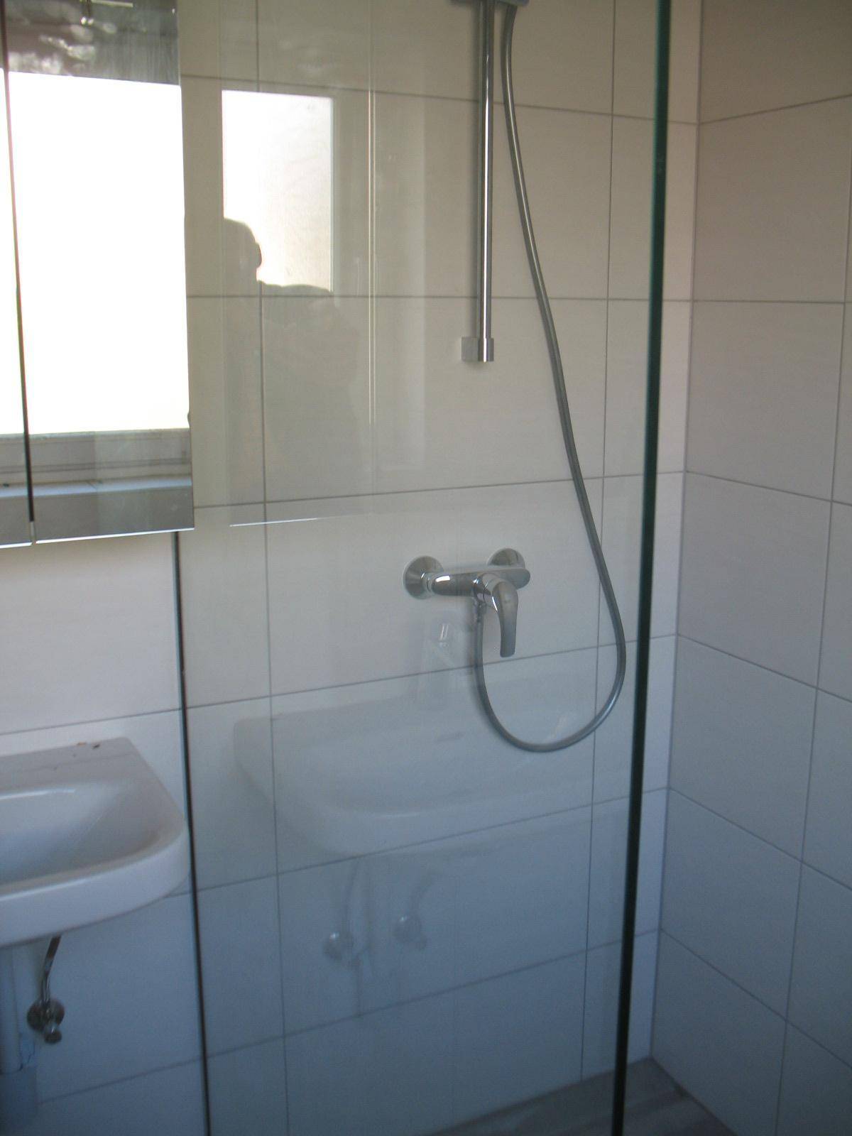 Duschbereich im Badezimmer mit weißen Fliesen und Glasabtrennung, modern und funktional.