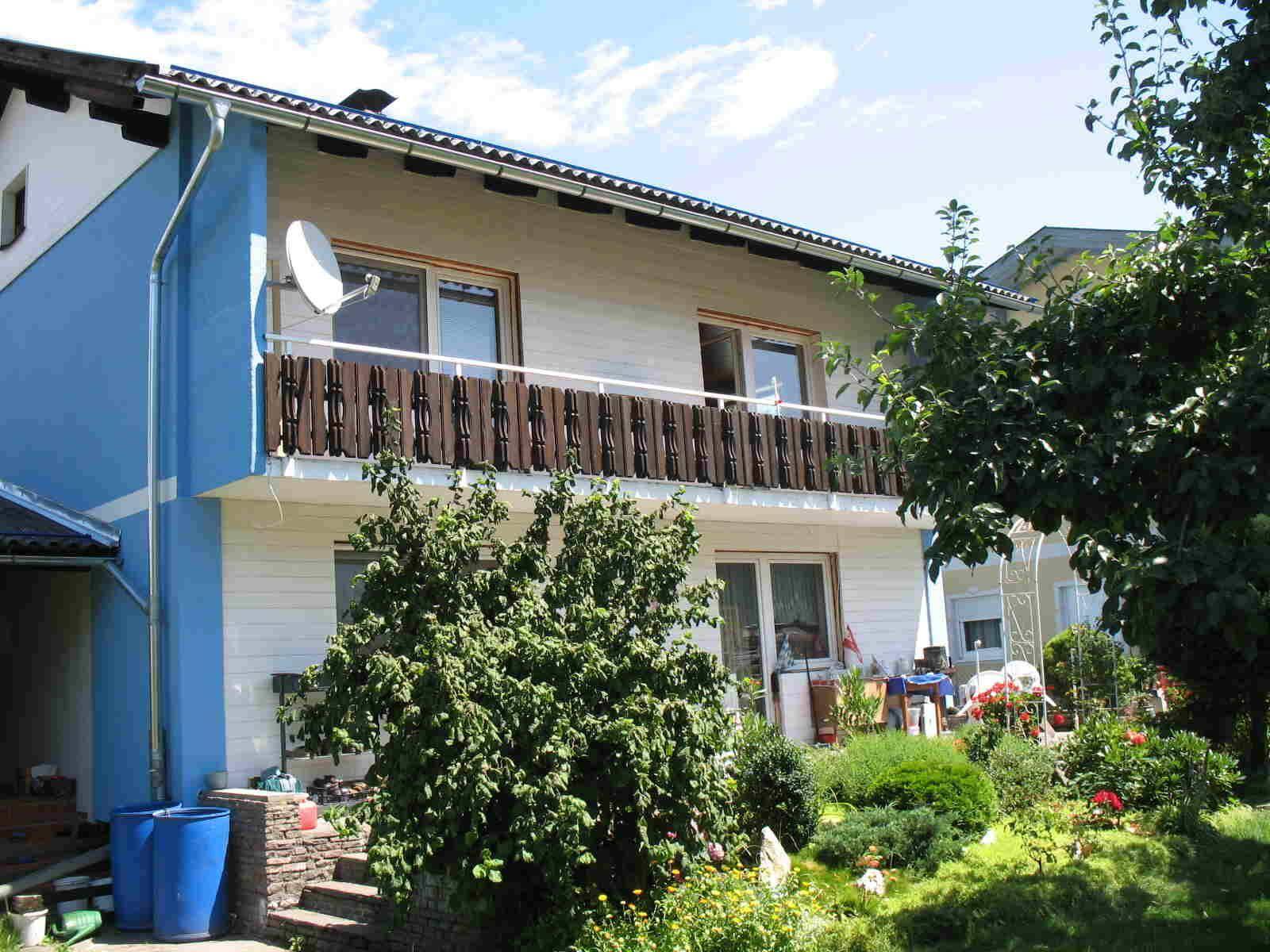Seitlicher Blick auf den Garten mit üppiger Bepflanzung und einem Balkon im ersten Stock.
