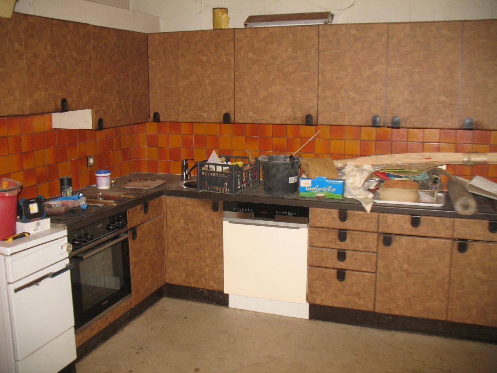 Veraltete Küche mit braunen Schränken, orangefarbenen Fliesen und sichtbaren Gebrauchsspuren.