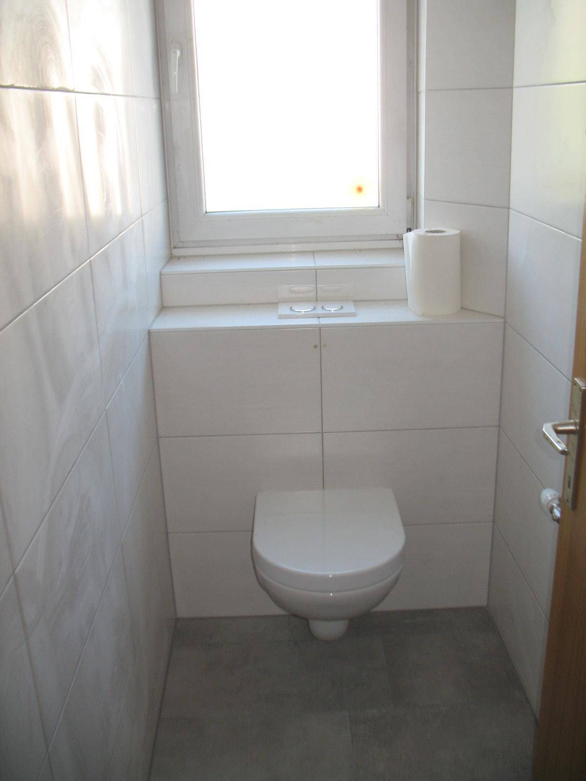 Separate Toilette mit wandhängendem WC, Fenster und weißen Fliesen, gut beleuchtet.