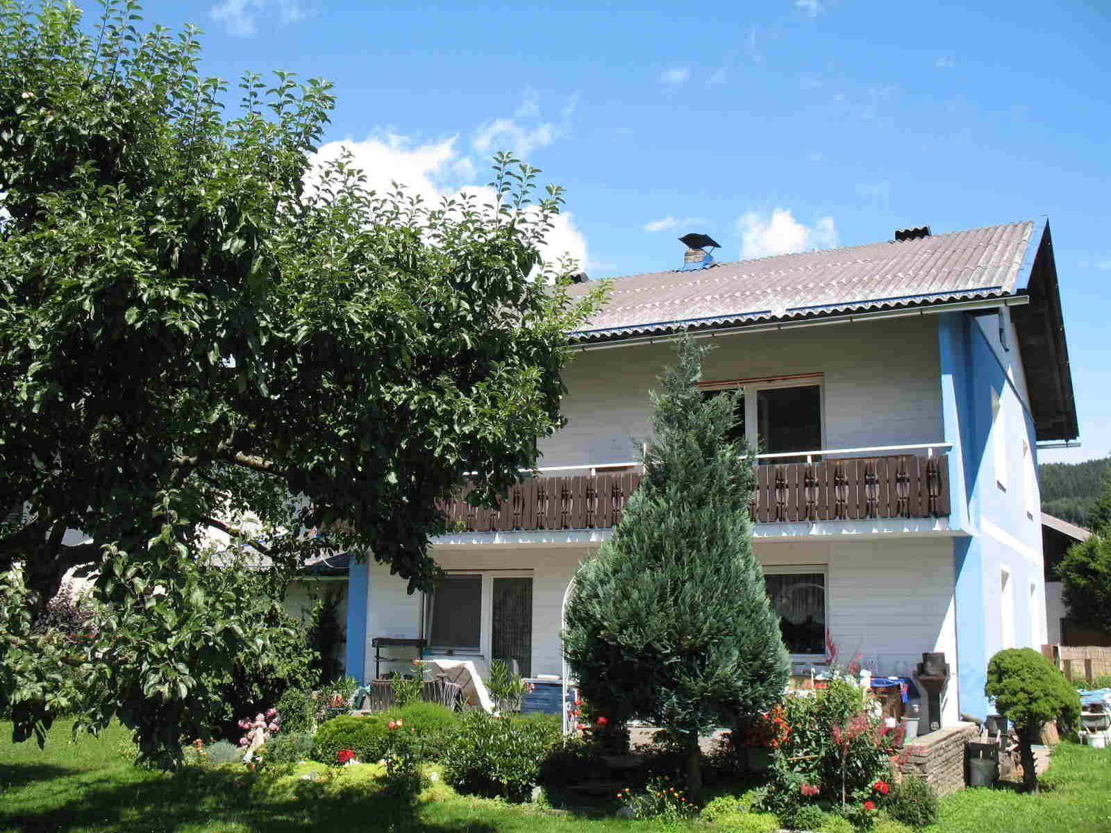 Grüner Gartenbereich hinter dem Haus mit Bäumen, Sträuchern und einem Balkon im Obergeschoss.