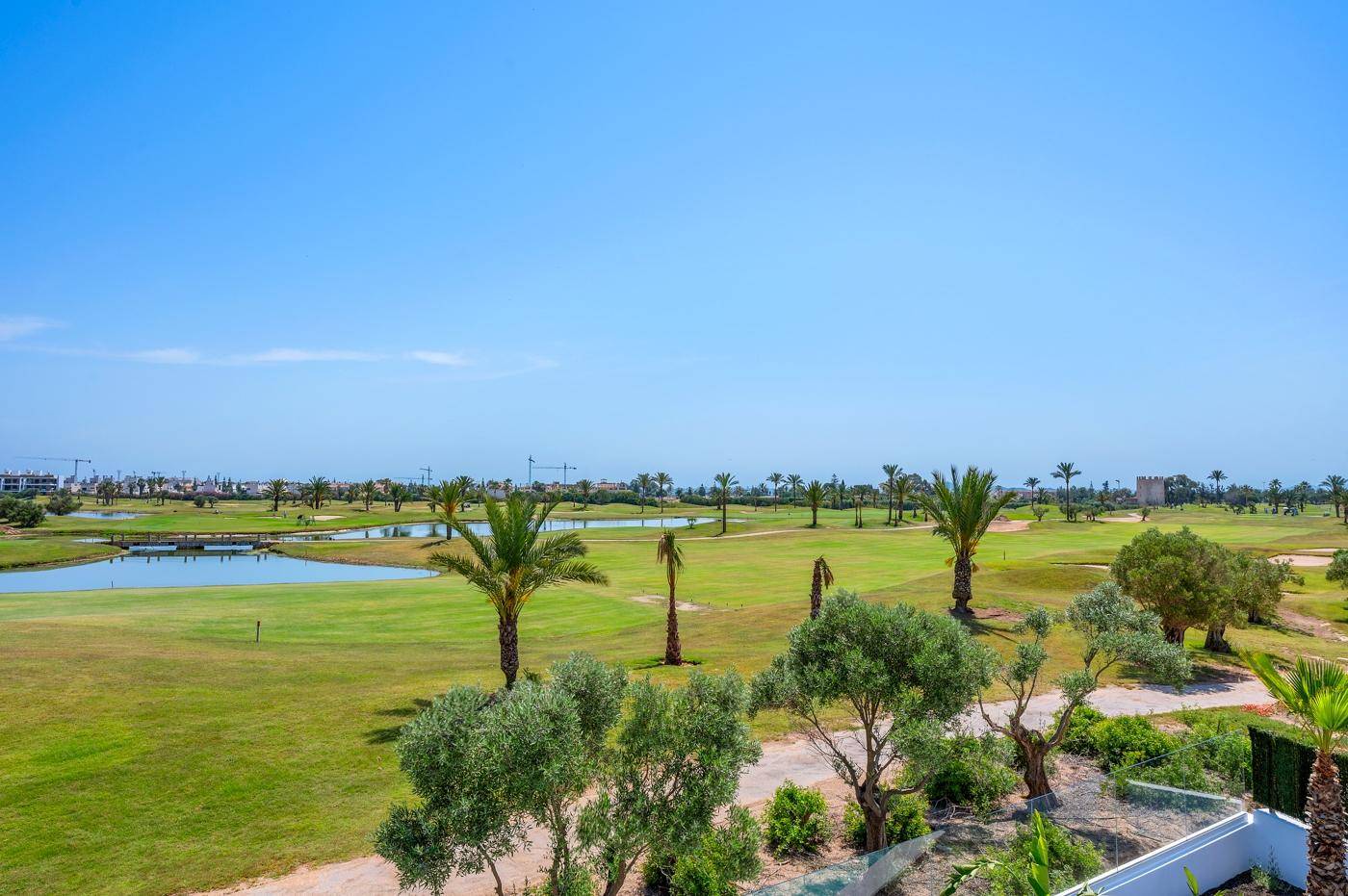 Panoramablick auf einen weitläufigen Golfplatz mit Seen und Palmen.
