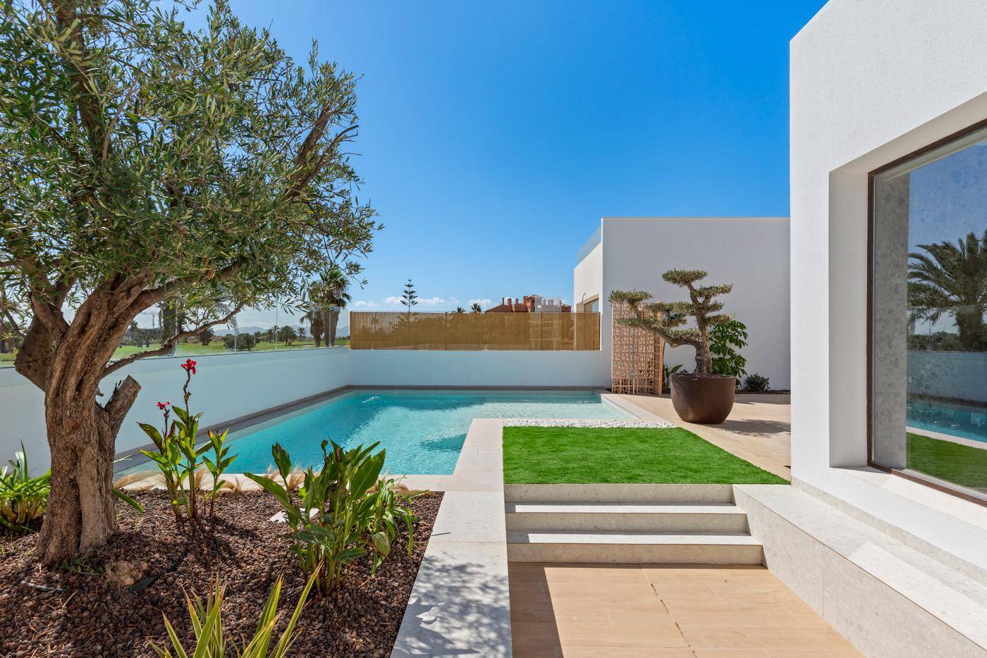 Sonniger Außenbereich mit Pool, Stufen zur Terrasse und mediterraner Bepflanzung.