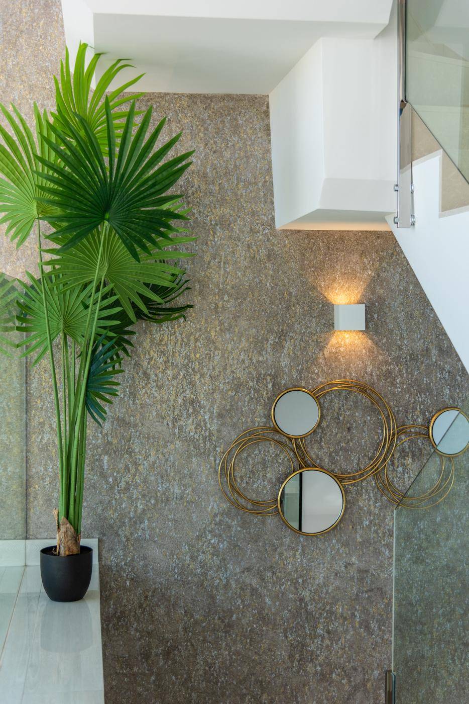Heller Flurbereich mit dekorativer Wandgestaltung, Pflanzen und Treppe mit Glasgeländer.
