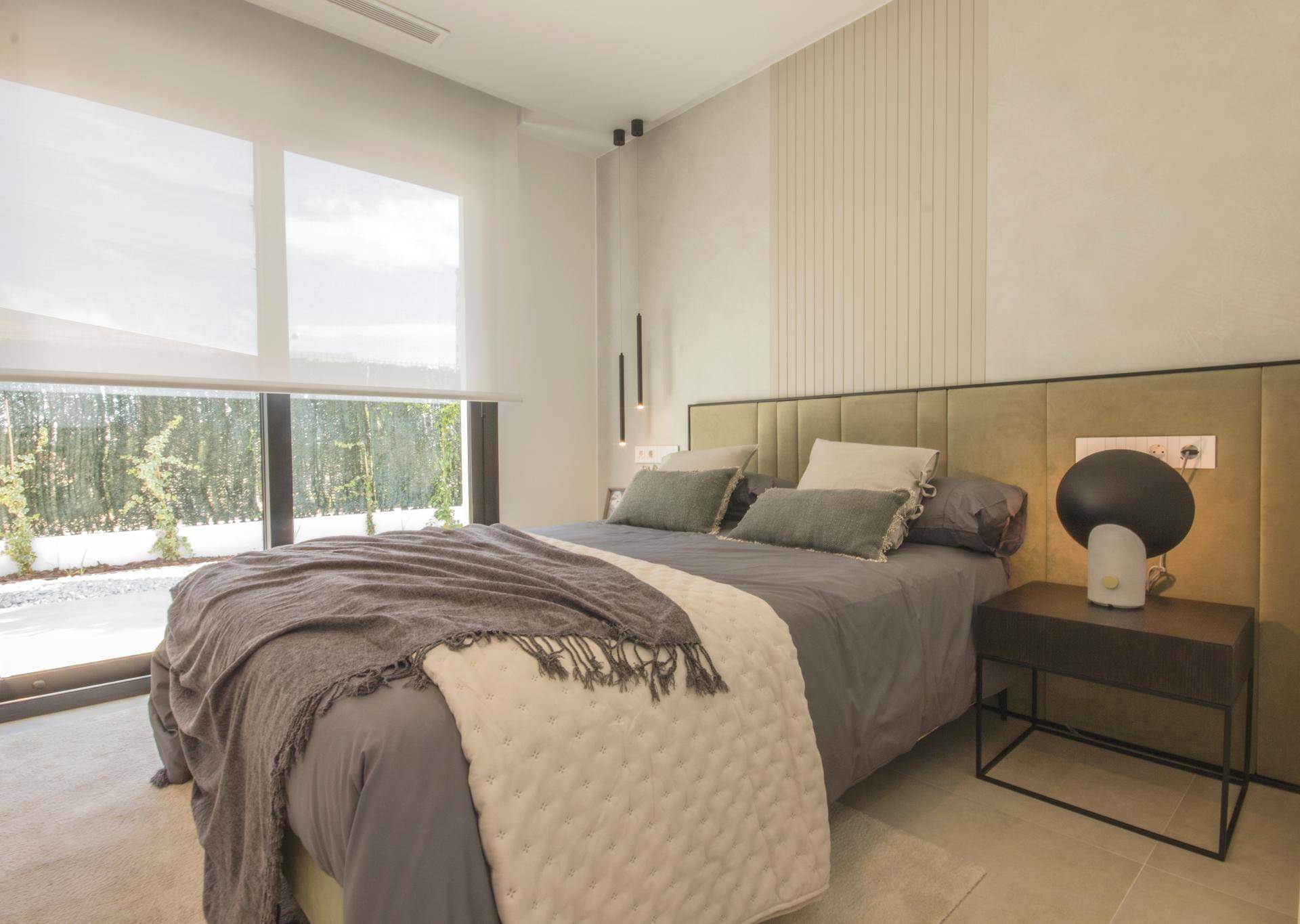 Helles Schlafzimmer mit großem Fenster, modernem Bett und minimalistischer Einrichtung.