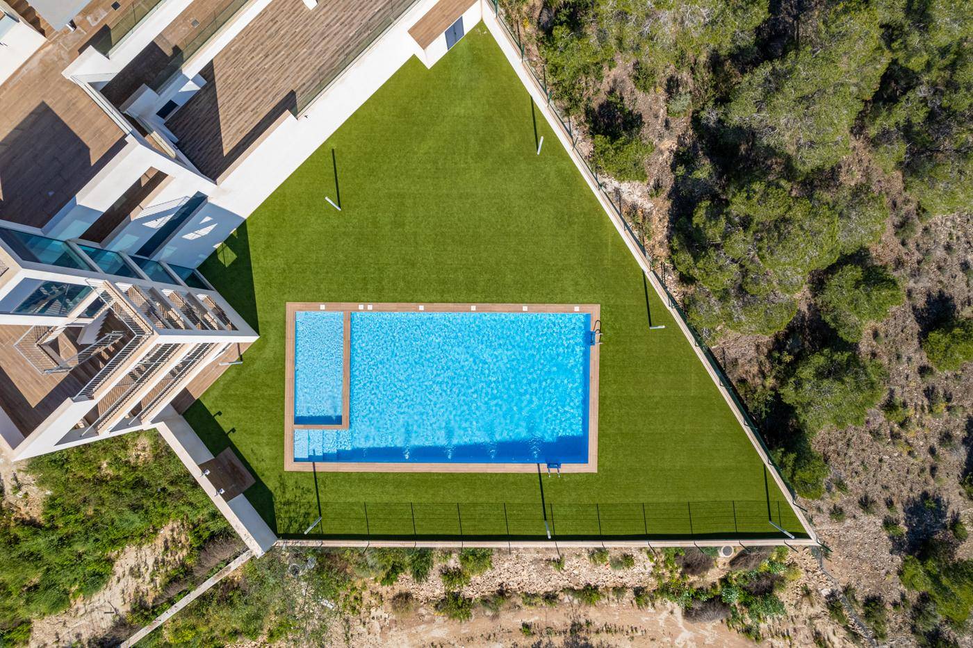 Großer rechteckiger Pool mit Kunstrasenfläche in einer modernen Wohnanlage.