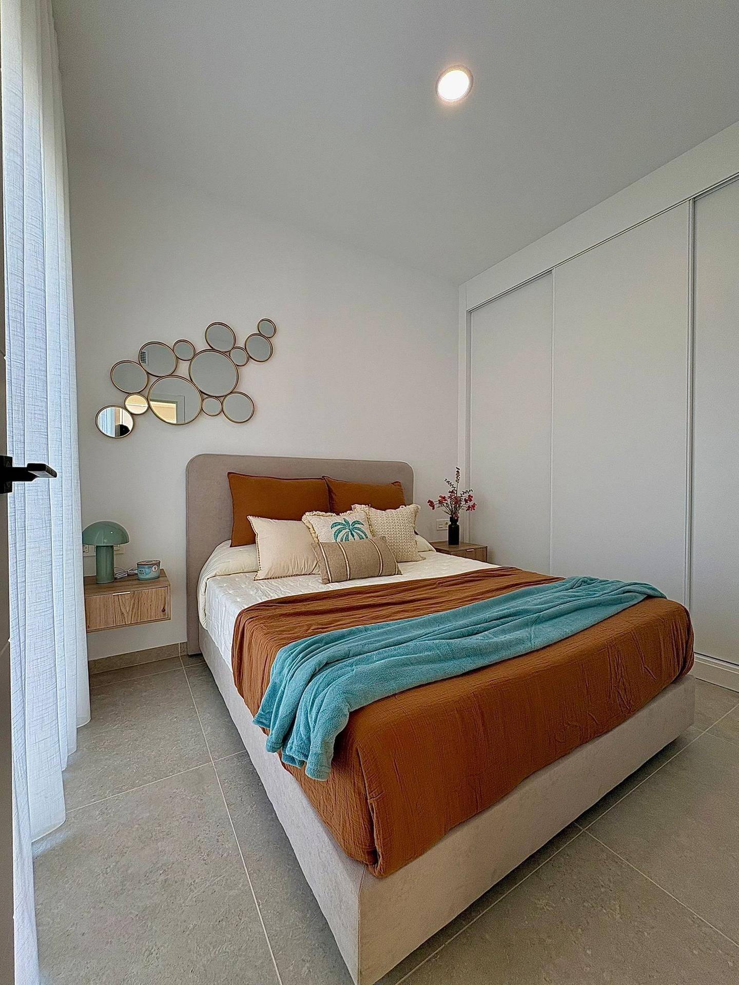 Helles Schlafzimmer mit Doppelbett, integriertem Kleiderschrank und modernen Spiegelelementen an der Wand.