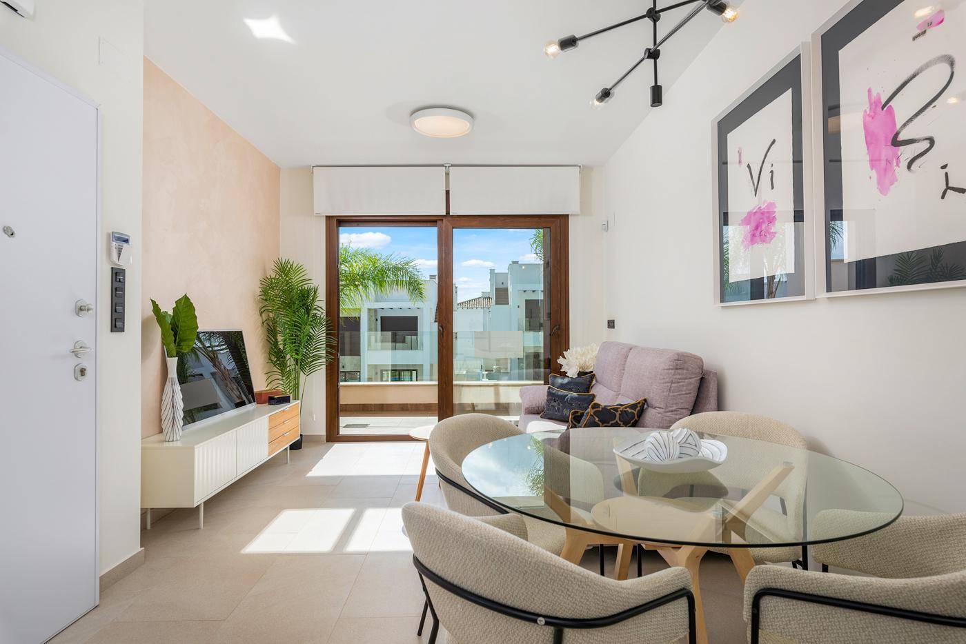 Offener Wohn- und Essbereich mit modernem Sofa, Glastisch und Zugang zu einem Balkon.