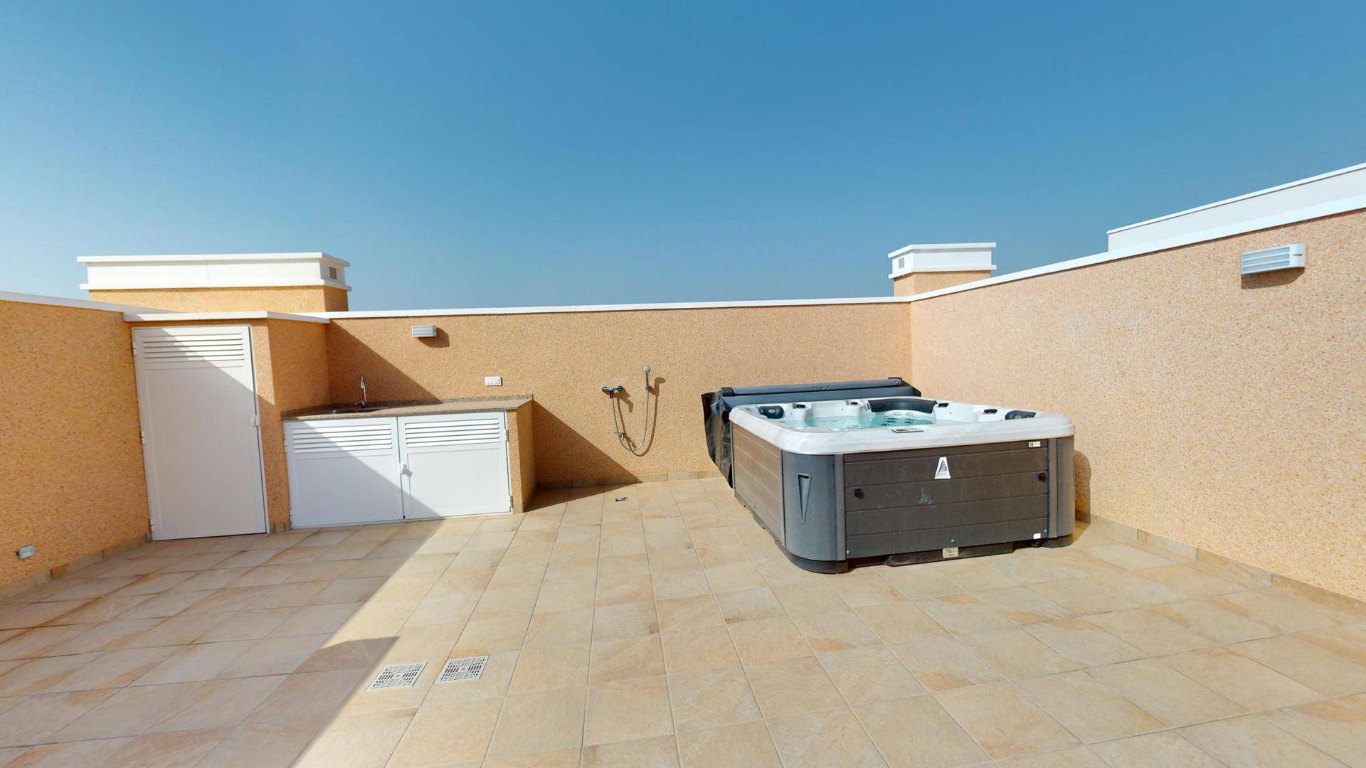 Große Dachterrasse mit Whirlpool und einer praktischen Außenküche unter blauem Himmel.