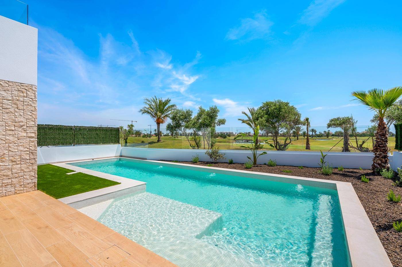 Sonniger Poolbereich mit Holzterrasse und Blick auf die weite grüne Landschaft unter blauem Himmel.