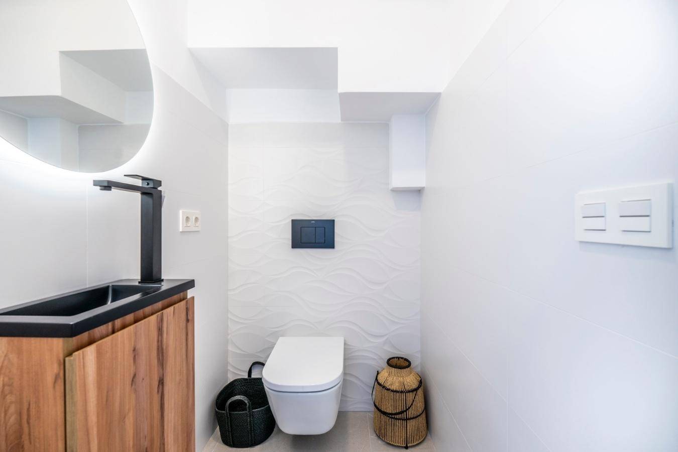 Modernes Gäste-WC mit Wand-WC, schwarzem Aufsatzwaschbecken und beleuchtetem Spiegel.