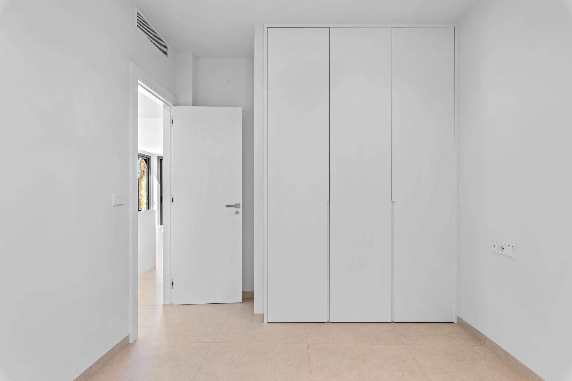 Geräumiges Schlafzimmer mit weißen Einbauschränken und Zugang zu einem weiteren Raum.