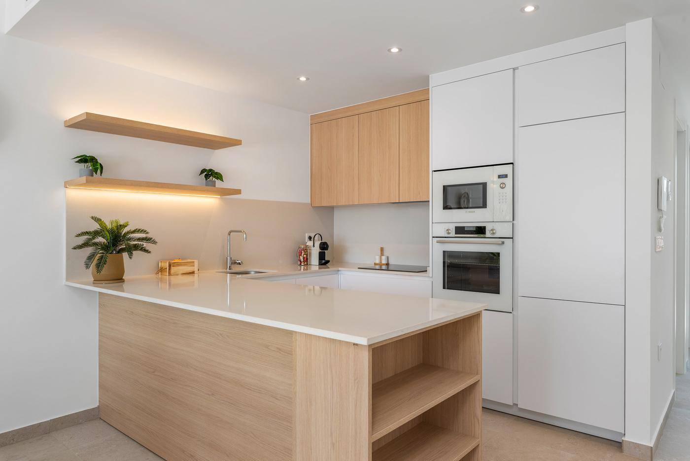 Offene, moderne Küche mit Kücheninsel, weißen Schränken und Holzdetails, gut beleuchtet.