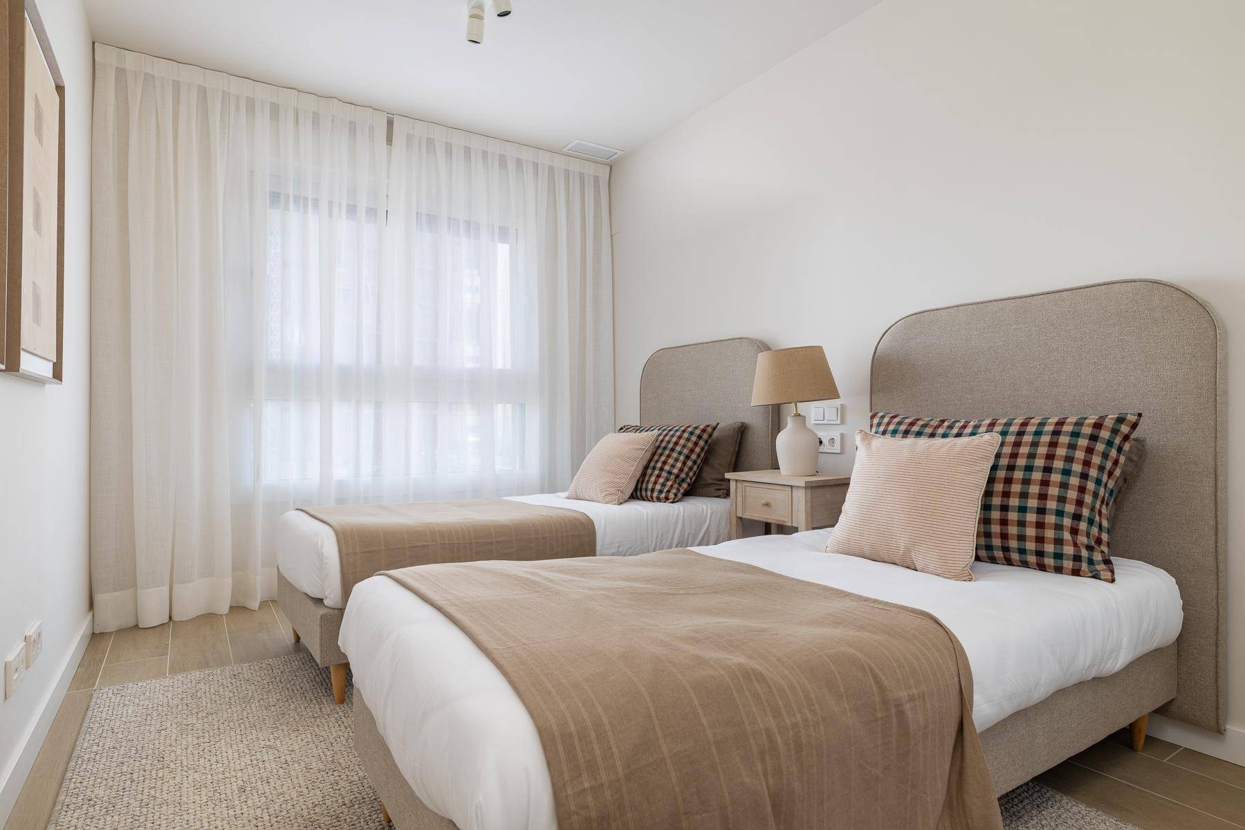Helles Schlafzimmer mit zwei Einzelbetten, beigen Textilien und Fenster mit Vorhängen.