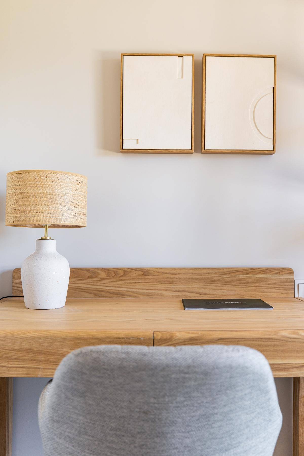 Detailaufnahme eines Holzschreibtisches mit einer modernen Lampe und gerahmten Bildern an der Wand.