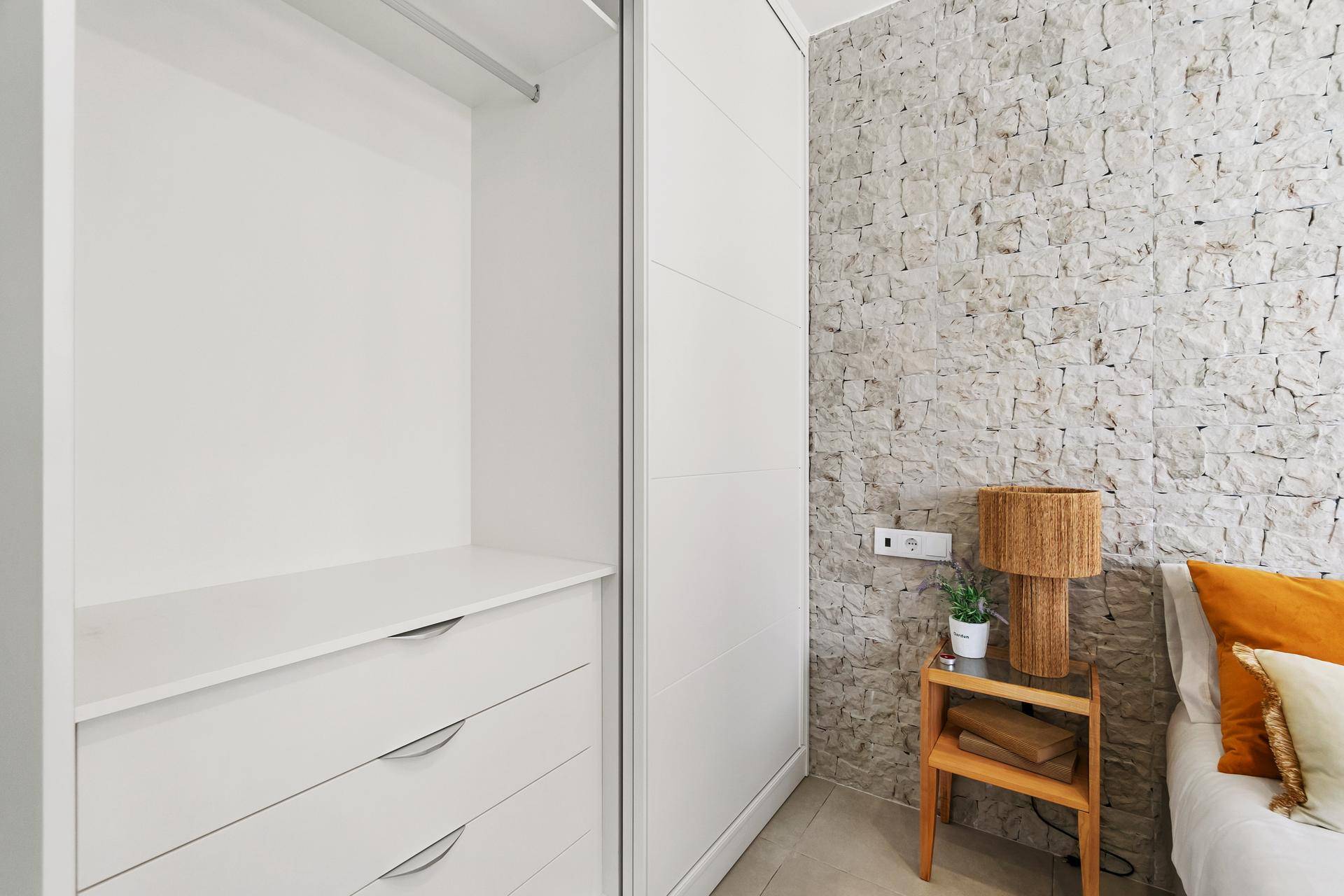 Schlafzimmer mit integriertem weißen Kleiderschrank und einer strukturierten Steinwand als Akzent.