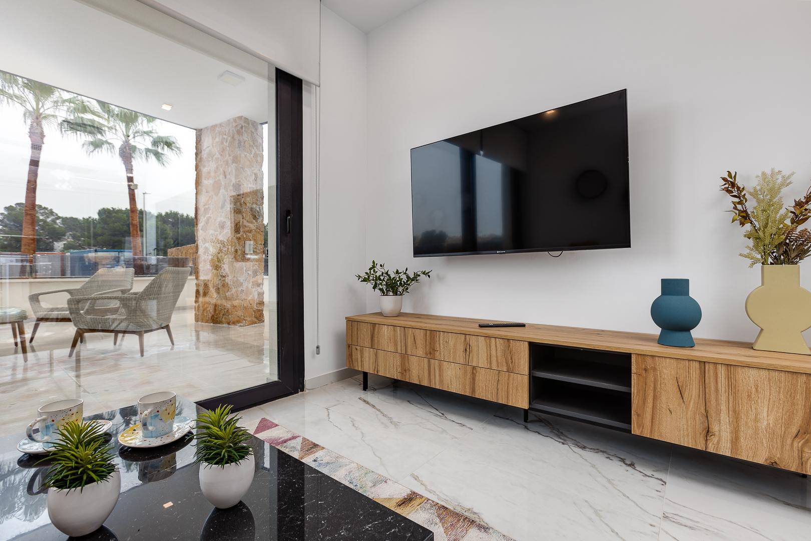 Helles Wohnzimmer mit Wandfernseher und großen Schiebetüren zur Außenterrasse.
