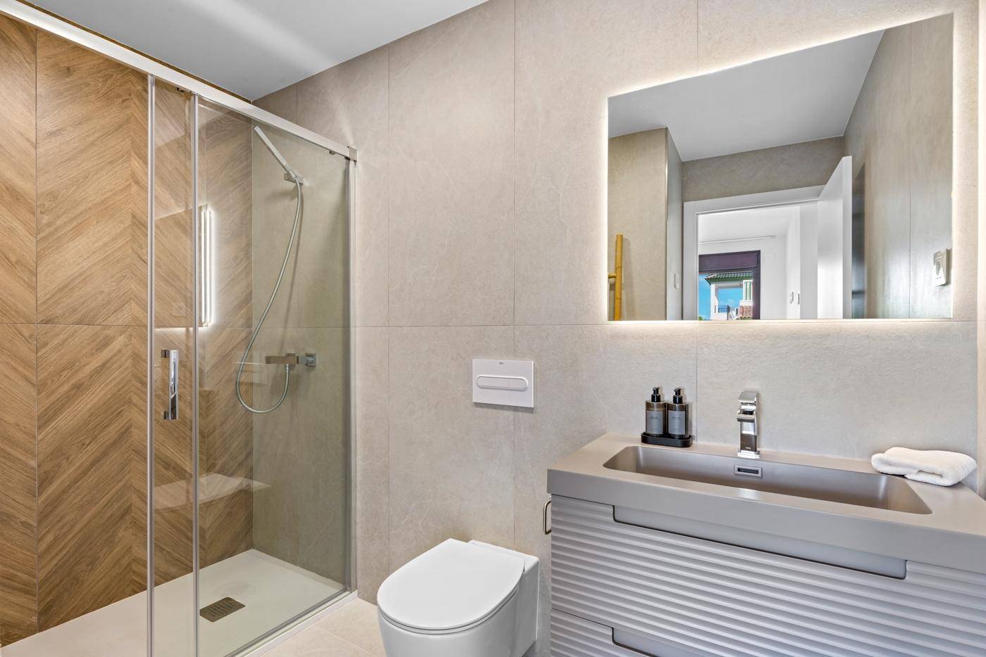Helles Badezimmer mit moderner Dusche, beleuchtetem Spiegel und Einzelwaschbecken.