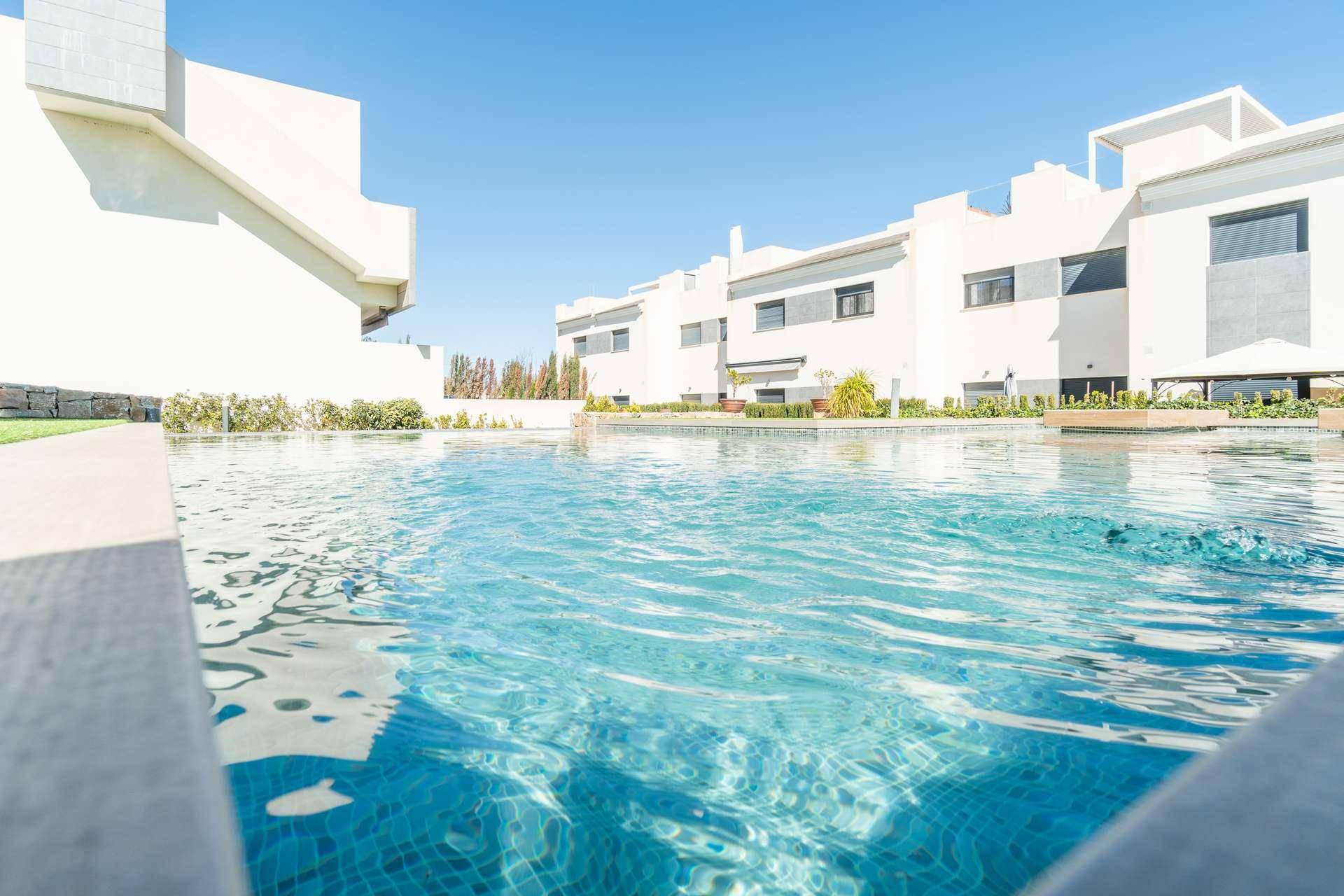 Nahaufnahme des Pools mit blauen Mosaikfliesen und moderner Architektur im Hintergrund.