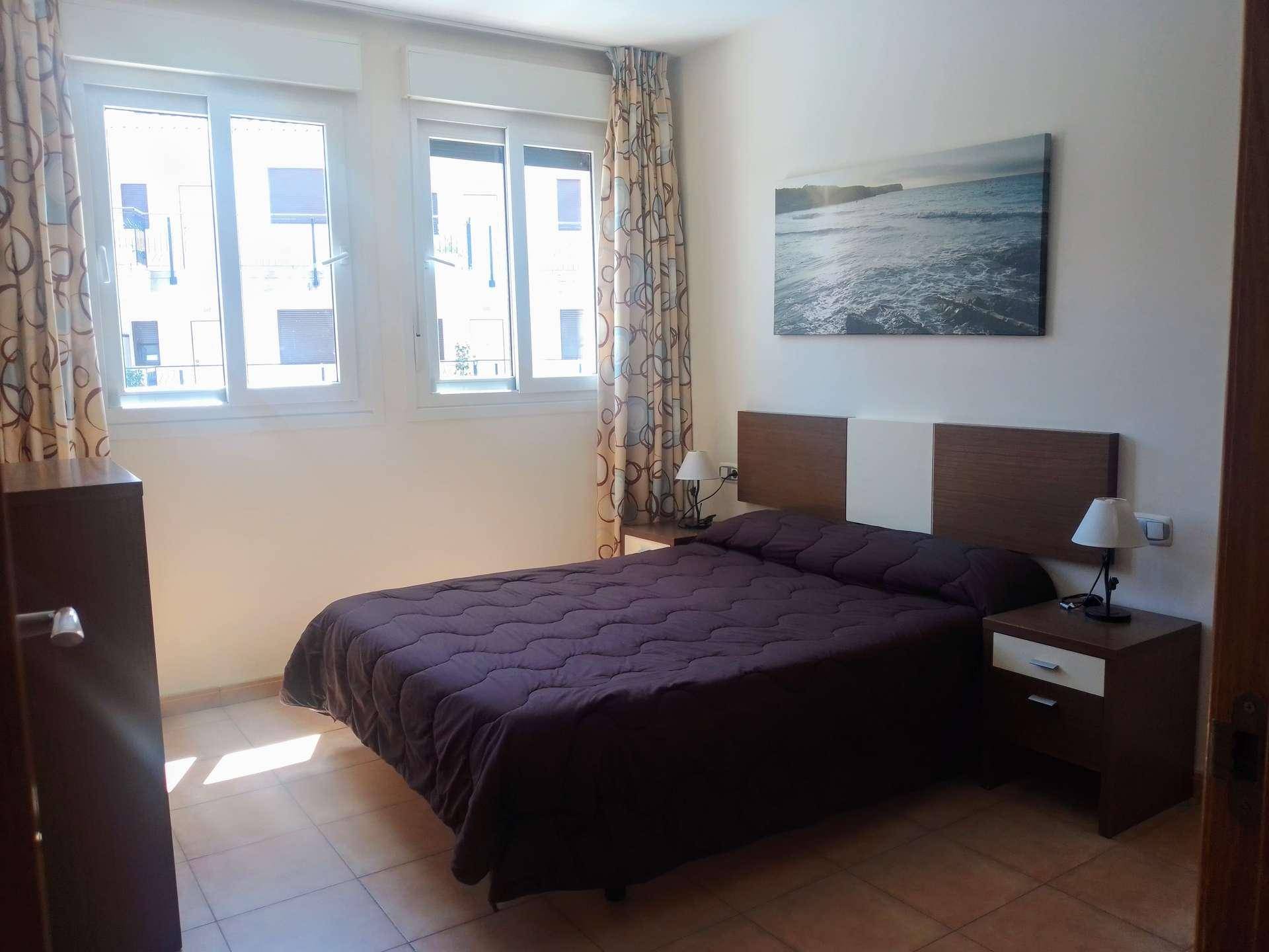 Schlafzimmer mit Doppelbett, Fliesenboden und großen Fenstern für viel Tageslicht.