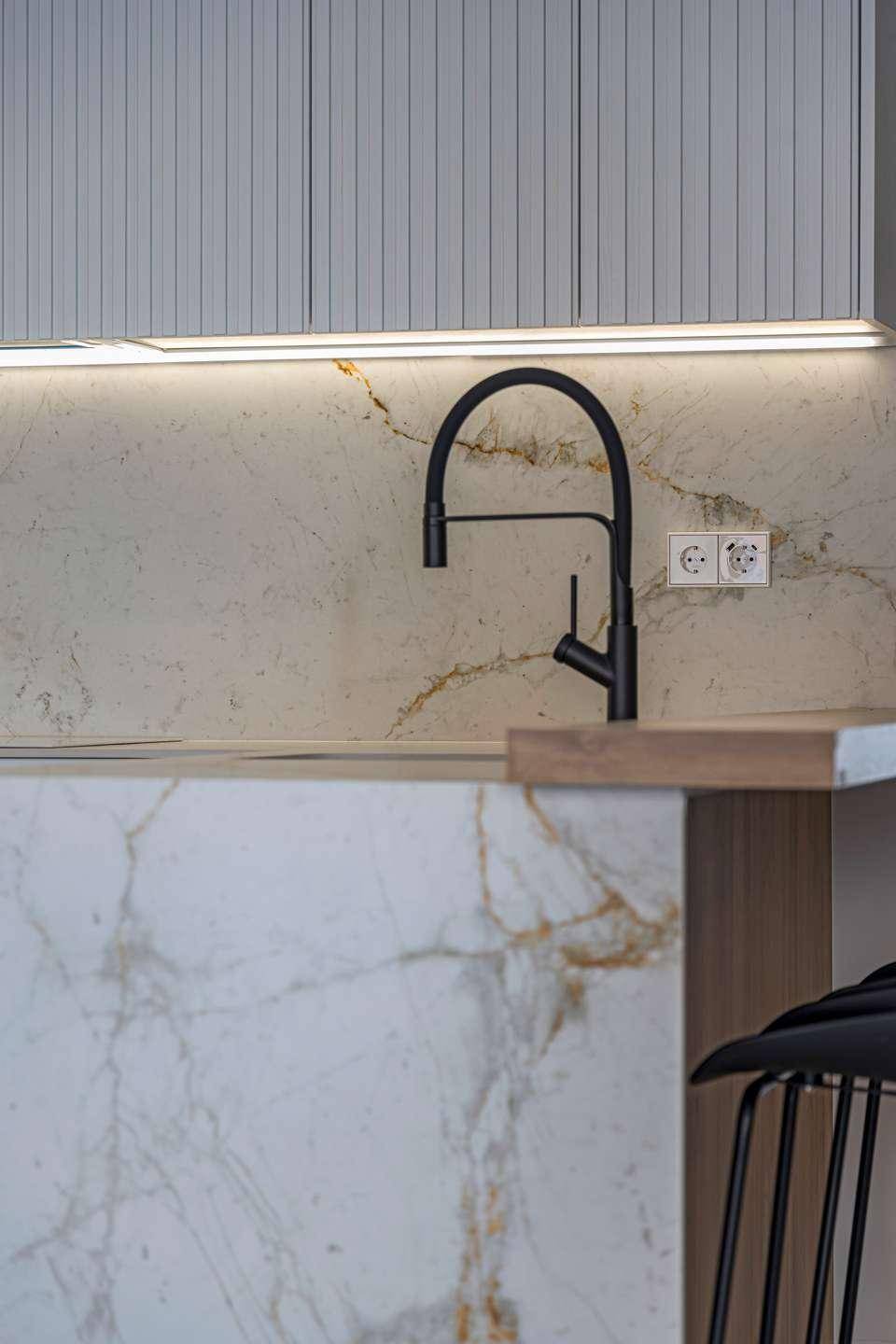 Detailaufnahme der Küchenspüle mit modernem schwarzem Wasserhahn und Marmorarbeitsplatte.