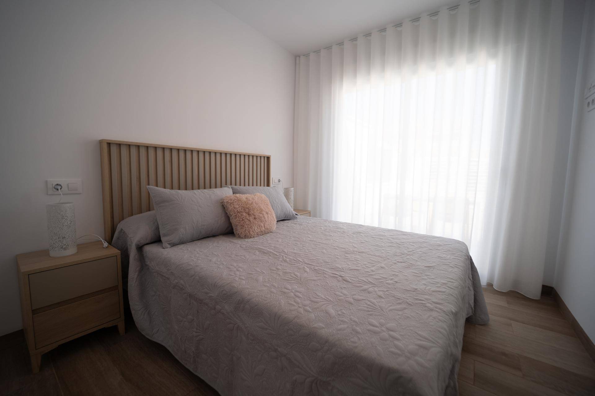 Helles Schlafzimmer mit Doppelbett, Holzkopfteil und modernem Laminatboden.