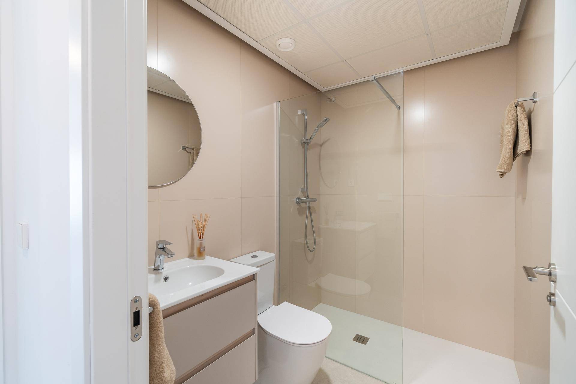 Modernes Badezimmer mit beigefarbenen Fliesen, ebenerdiger Dusche und Waschtisch mit Spiegel.