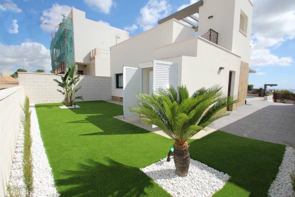 Moderner Garten mit Kunstrasen, Palmen und weißer Steinumrandung neben dem Haus.