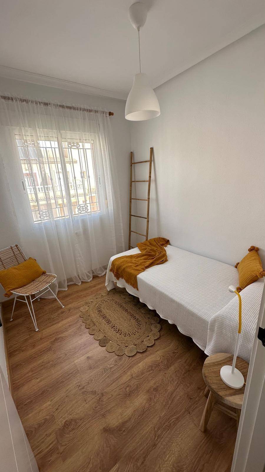 Helles Schlafzimmer mit Einzelbett, Holzboden und einem runden Teppich.