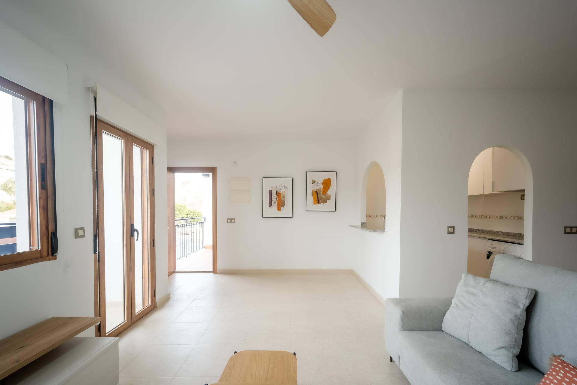 Helles Wohnzimmer mit Fliesenboden, Zugang zum Balkon und einem Durchgang zur Küche.