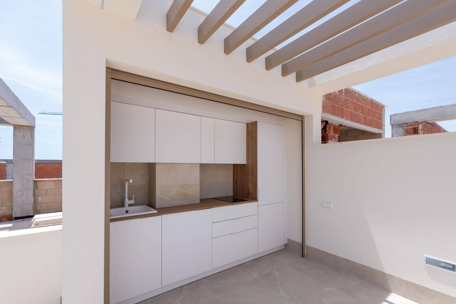 Moderne Außenküche auf einer Dachterrasse mit weißen Schränken und Holzarbeitsplatte.