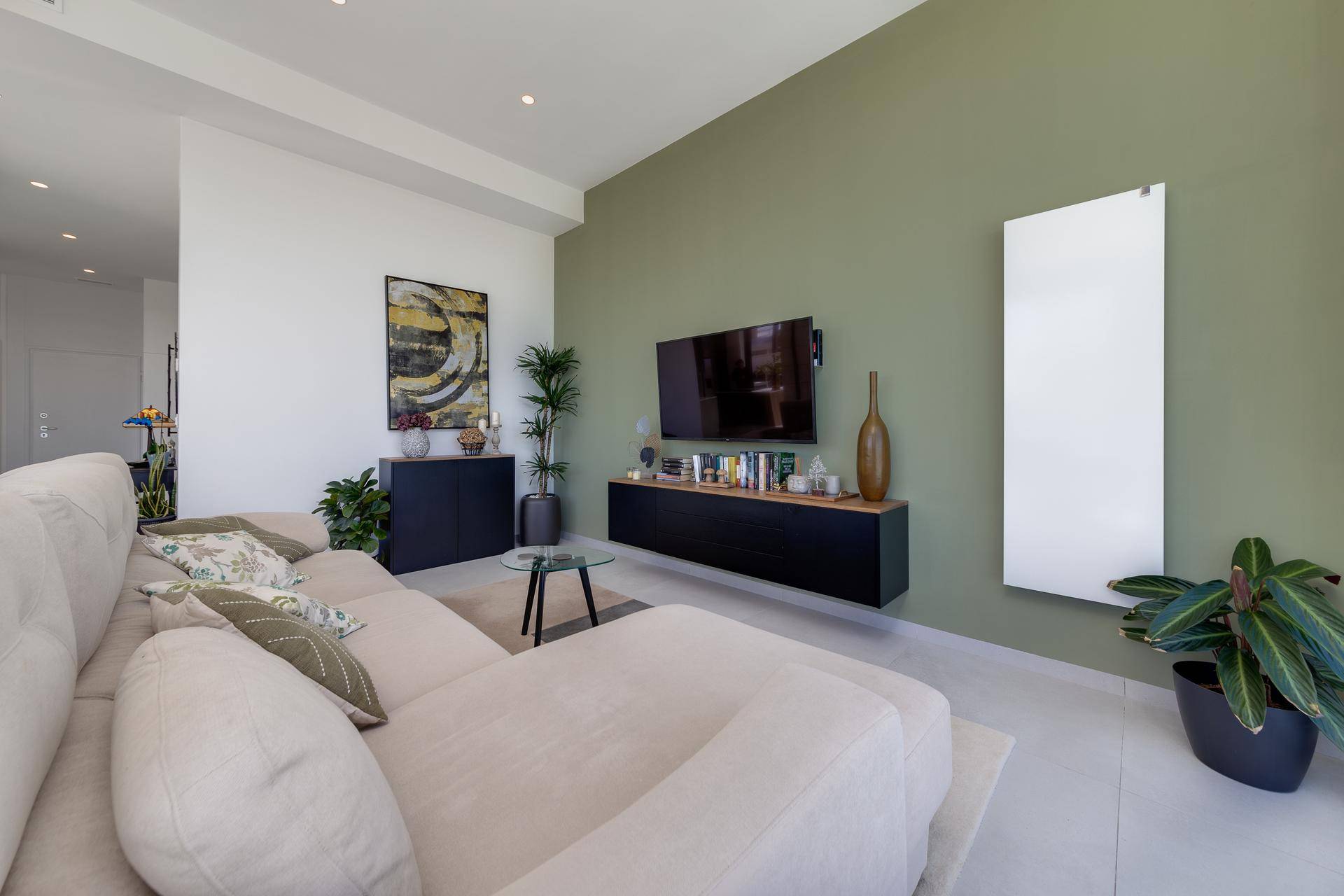 Heller Wohnbereich mit beigem Sofa, grüner Akzentwand und modernen Möbeln.