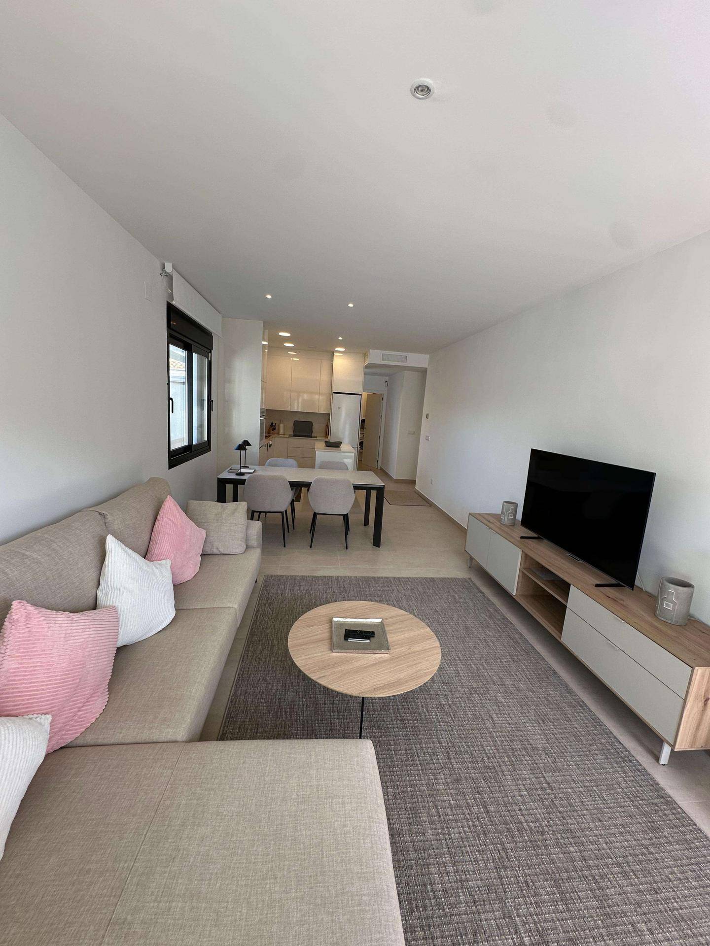 Offener Wohnbereich mit beigem Sofa, Teppich und Blick auf den Ess- und Küchenbereich.