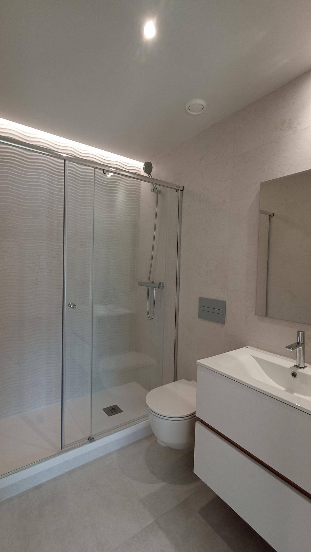 Helles Badezimmer mit moderner Duschkabine, WC und Waschtisch mit Spiegel.