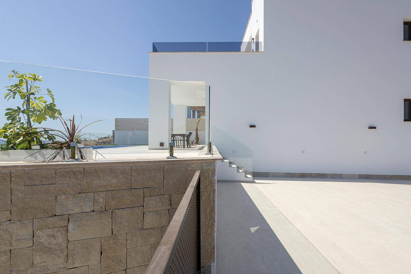 Moderne weiße Fassade mit Außentreppe und Glasgeländer in sonniger Umgebung.