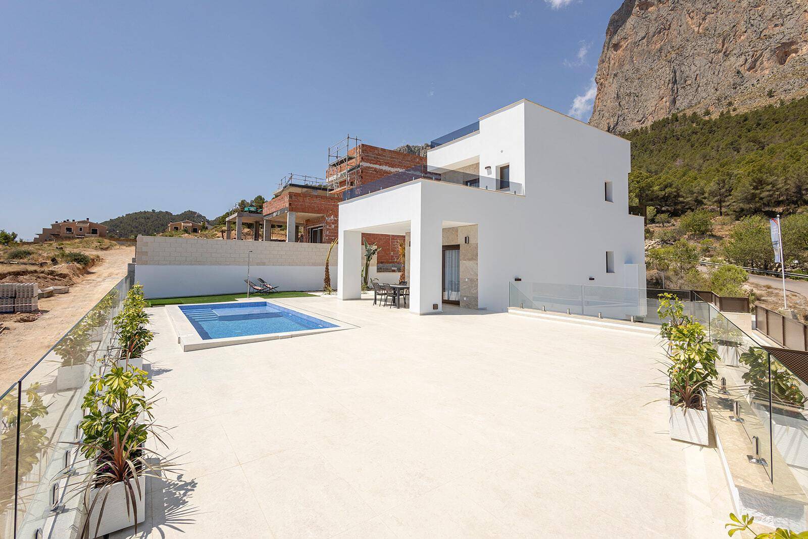 Moderne Villa mit Pool und großer Sonnenterrasse, umgeben von Baustellen und Natur.