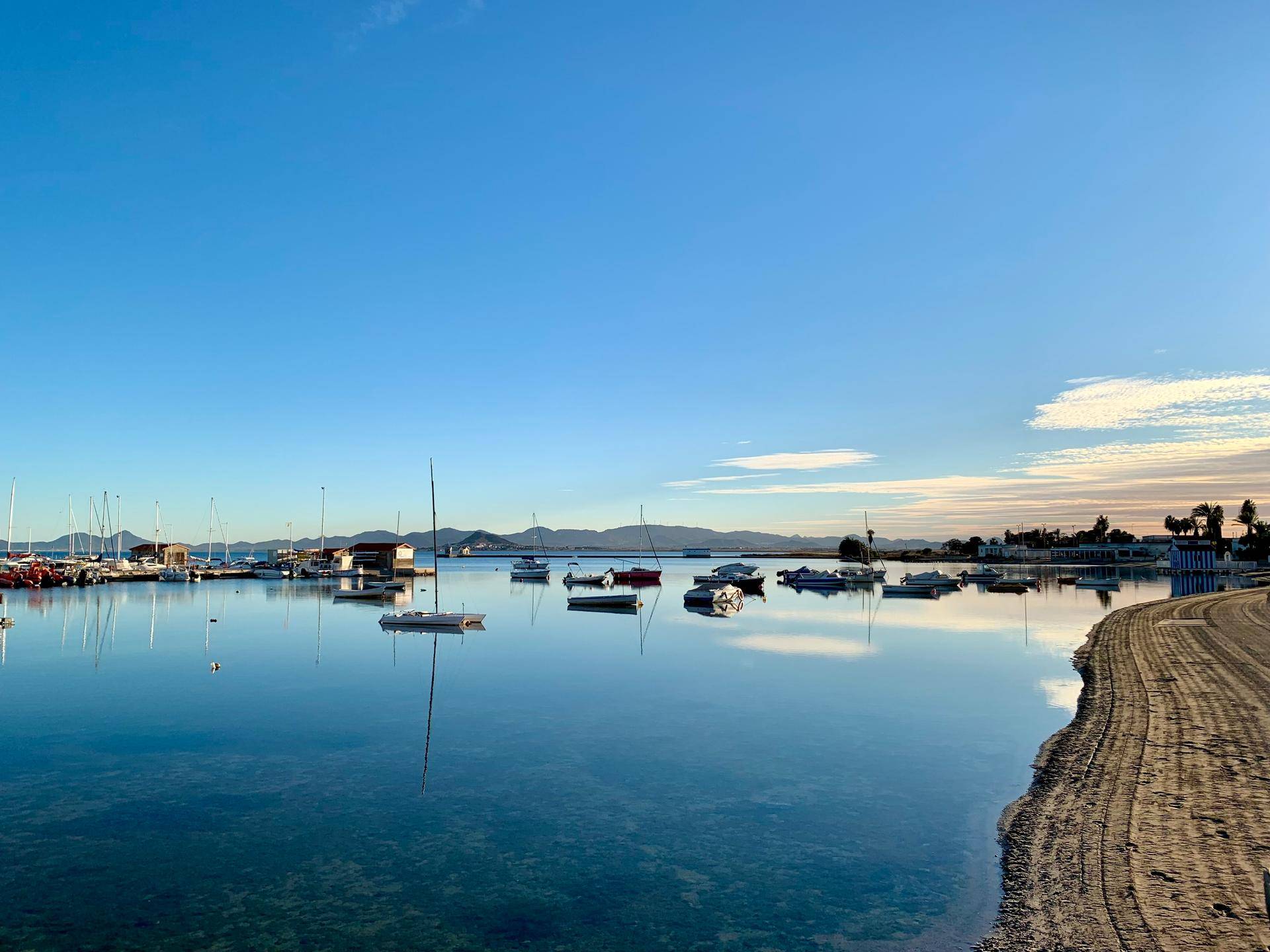 Ruhige Bucht mit zahlreichen Booten, spiegelndem Wasser und Bergen am Horizont.