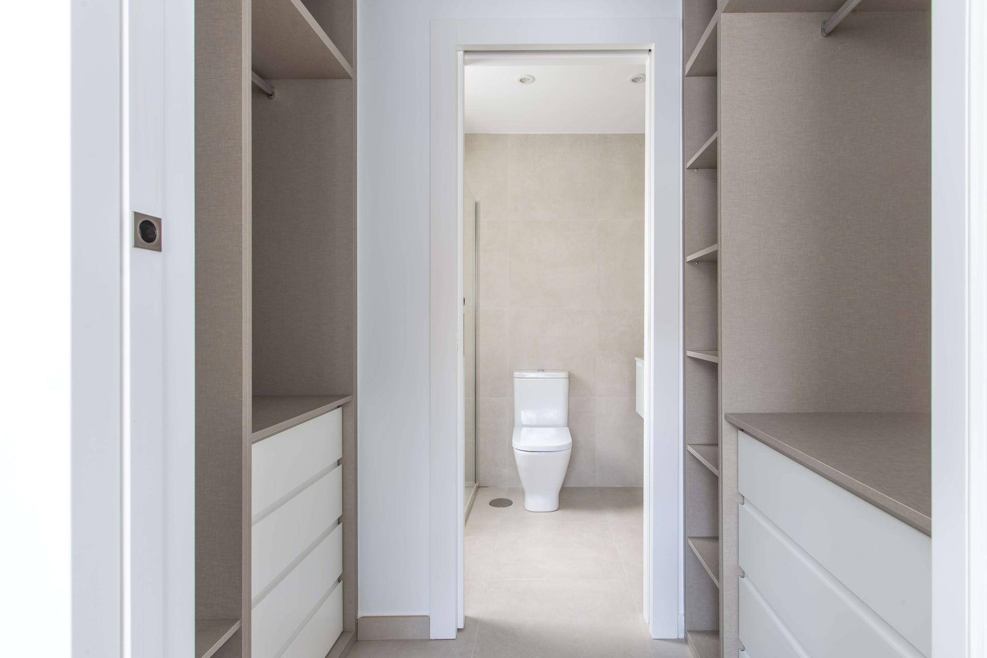 Begehbarer Kleiderschrank mit offenen Regalen und Schubladen, der zum Badezimmer führt.